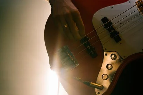 Close-up of a hand plucking strings on an electric bass guitar body with knobs Stock Photos