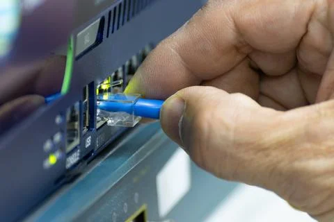 Close-up of a hand plugging a blue ethernet cable into a network switch or .. 스톡 사진