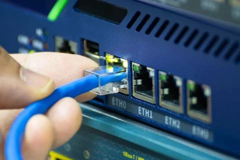 Close-up of a hand plugging a blue ethernet cable into a network switch or .. 스톡 사진