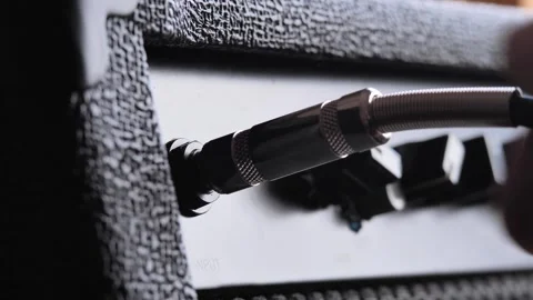 Close-up hand plugging guitar jack cable into black amplifier Stock Footage 321890727