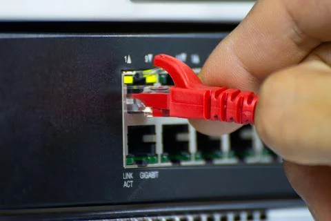 Close-up of a hand plugging a red ethernet cable into a network switch or r.. Stock Photos