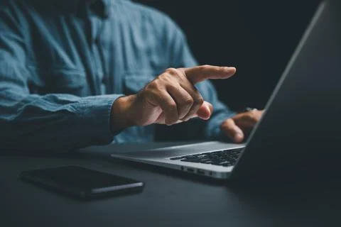 Close-up of a hand pointing at a laptop screen, with a smartphone lying on .. Stock Photos