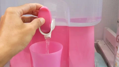 Close up hand pouring fresh drinking water from a pink plastic dispenser Stockbeeldmateriaal 333443283