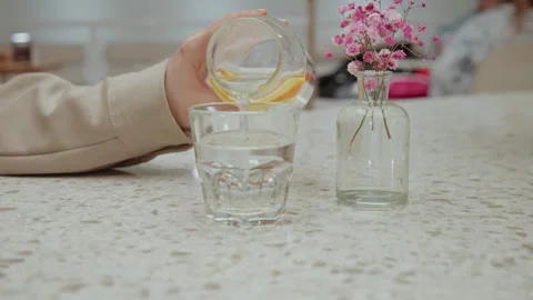 Close up of hand pouring lemon infused water from glass bottle into drinking Stock Footage 345063154