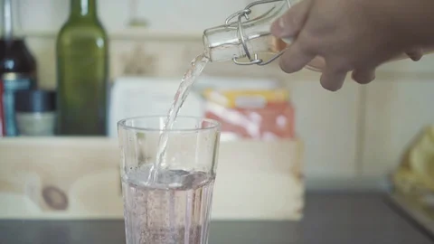 Close up of hand pouring lemonade or water into a glass cup. Drinking in kitchen Stockbeeldmateriaal 103117320