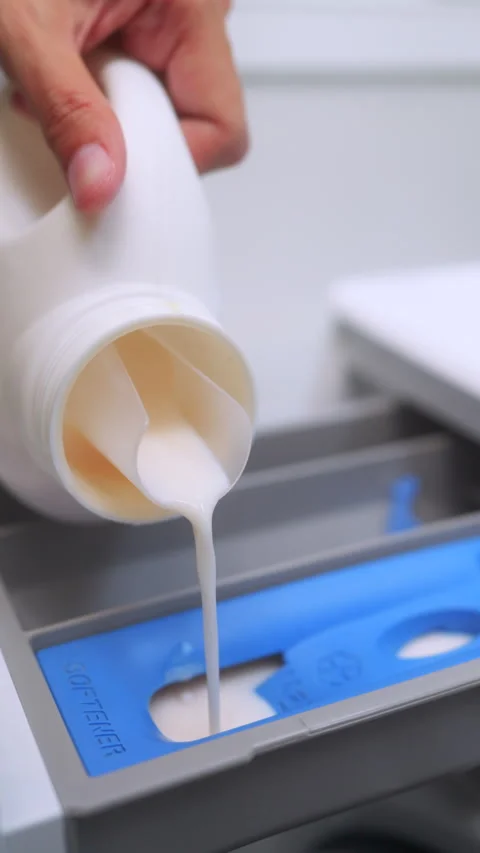 Close up of a hand pouring liquid fabric softener into the washing machine. Video stock 328923906