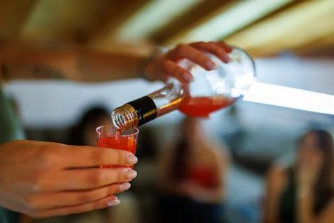 Close-Up of a Hand Pouring a Red Liquid from a Bottle into a Clear Plastic Cup Foto stock