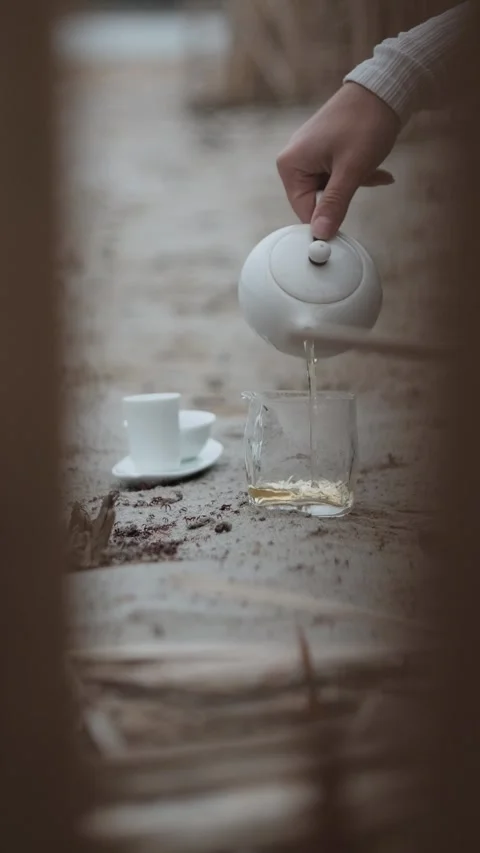 Close-up of hand pouring warm tea on the sand near reeds by a lake, during a Stock Footage 307756828