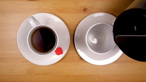 Close up hand pours cup of coffee with bubbles beside steeping cup of tea. Stock Footage 86535992