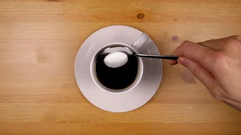 Close up as hand pours sugar into a cup of coffee on wood table. Stock-Footage 86537486