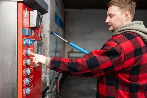 Close up of a hand pressing a button on a self-service coin machine at car wash. Stock Photos