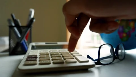 Close-up of a hand pressing a calculator button on a desk with glasses and pe Stock Footage 316800031