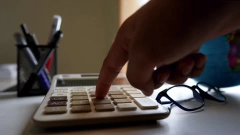 Close-up of a hand pressing a calculator button on a desk with glasses and pe Stock Footage 318056917
