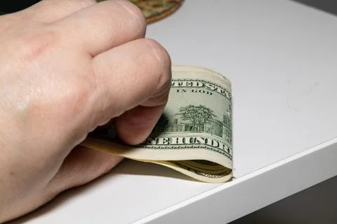Close-up of a hand pressing down a stack of hundred-dollar bills on a white.. Stock Photos