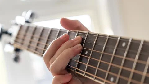 Close-up of a hand pressing guitar strings on the fretboard, with a blurred Stock-Fotos