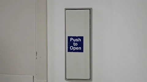 Close-up of a hand pressing a “Push to Open” button on a wall-mounted door 動画素材 333537876