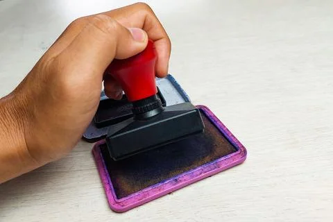 Close up of a hand pressing a rubber stamp onto an ink pad on a desk. Stock Photos