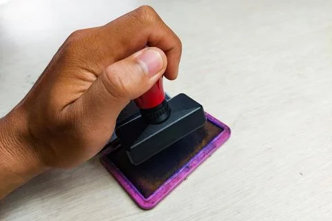 Close up of a hand pressing a rubber stamp onto an ink pad on a desk. Stock Photos