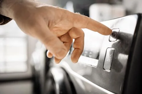 Close-up of a hand pressing the start button on a modern washing machine, s.. Stock Photos