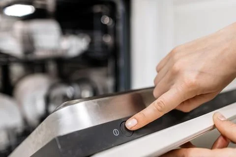 Close-up of a hand pressing the start button on a modern dishwasher, showca.. Stock Photos