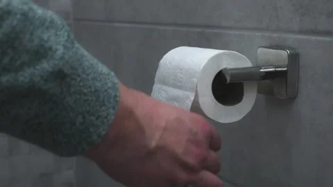 A close-up of a hand pulling a sheet from a toilet paper roll mounted on a Stock Footage 301541093