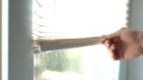 Close up of a hand pulling up white pleated window blinds to let daylight in Vidéo 340159341