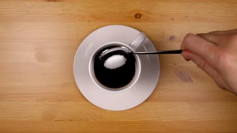 Close up as hand quickly pours sugar into a cup of coffee on wood table. Stock Footage 86536642