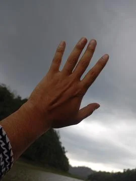 Close-up of a hand reaching towards a cloudy sky during daytime Stock Photos