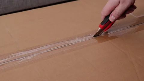 Close-up of a hand with a red box cutter slicing through packing tape on a .. Stock Footage 324964459