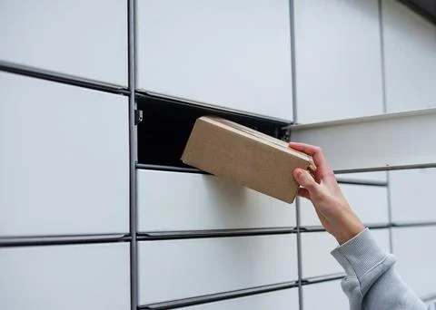 Close-up of a hand retrieving a cardboard parcel from automated locker. Conta Stock Photos
