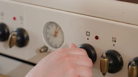 Close-up hand rotating oven control knob on white stove panel to adjust heat Stock-Footage 345657542