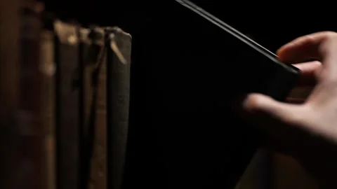Close-up of a hand selecting an old book from a dimly lit library shelf Stock Footage 345260137