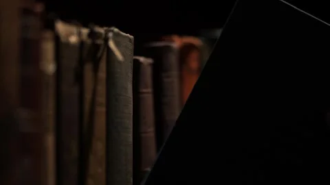 Close-up of a hand selecting an old book from a dimly lit library shelf Stock Footage 345260148