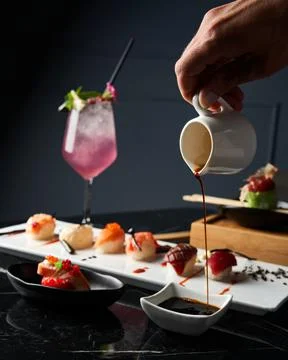 Close-up hand serving soy sauce. Detail of sushi set on wooden tray. Stock Photos