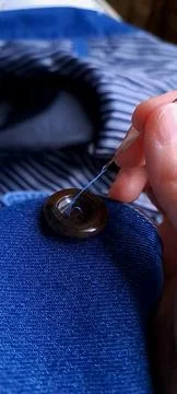 Close up of a hand sewing a brown button onto blue denim fabric Foto stock