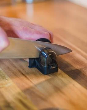 Close-up hand sharpening a knife with a handheld sharpener on a wooden surface Stock Photos