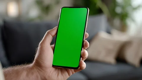 Close hand showcases green‑screen smartphone in a living room Video stock 317215874