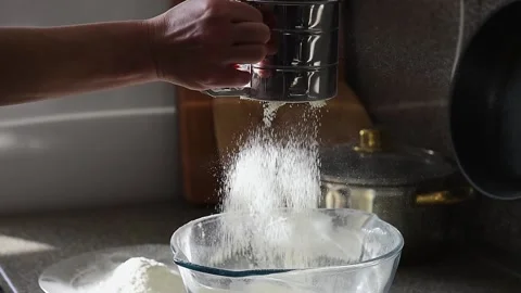 Close up of hand sifting white flour into glass bowl with a steel sieve. Stock Footage 169576960