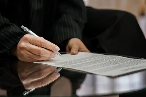 Close-Up of Hand Signing a Document on a Reflective Surface Stock Photos