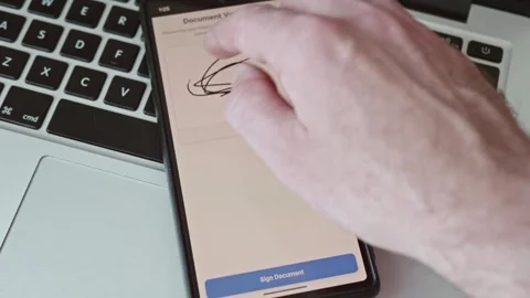 Close up of hand signing e-document via smartphone app on laptop background Stock Footage 337998856