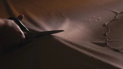 Close-up of a hand skillfully cutting fabric with sharp scissors in a dark room Stock Footage 266692718