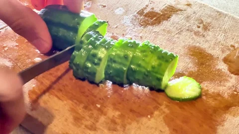 Close-Up of Hand Slicing Green Cucumber on Wooden Cutting Board Stock Footage 343432180