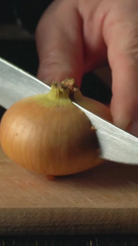 Close-up of hand slicing an onion with a sharp knife on a wooden cutting board, Stock Footage 339030571