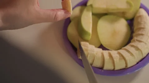 Close up hand slicing peeled bananas into small pieces on purple plate with Stock Footage 344410075