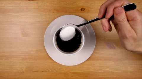 Close up as hand slowly pours sugar into a cup of coffee on wood table. Video stock 86537513