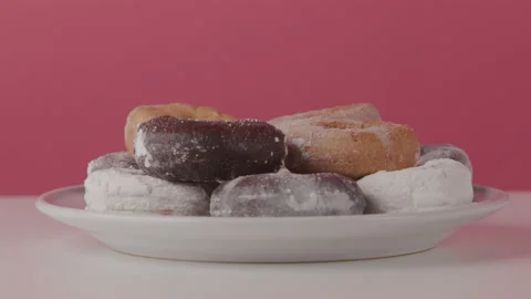 Close up of a Hand Sneaking a Donut From a Plate in Front of a Red Backdrop Stock Footage 208762611