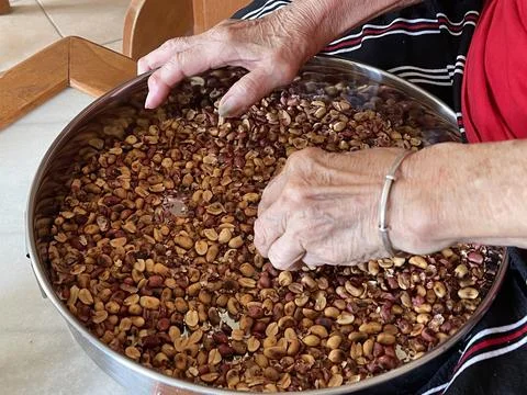 Close Up Of Hand Sorting Roasted Peanuts For Traditional Filling Preparation Foto stock