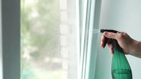 Close up of a hand spraying liquid glass cleaner from a green bottle onto a.. 스톡 동영상 340159380