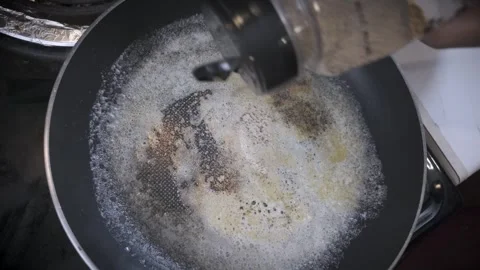 Close-up of a hand sprinkling pepper onto sizzling butter in a frying pan Stock Footage 294951298