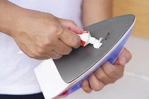 Close up hand squeeze toothpaste to clean stain on iron appliance surface Stock Photos